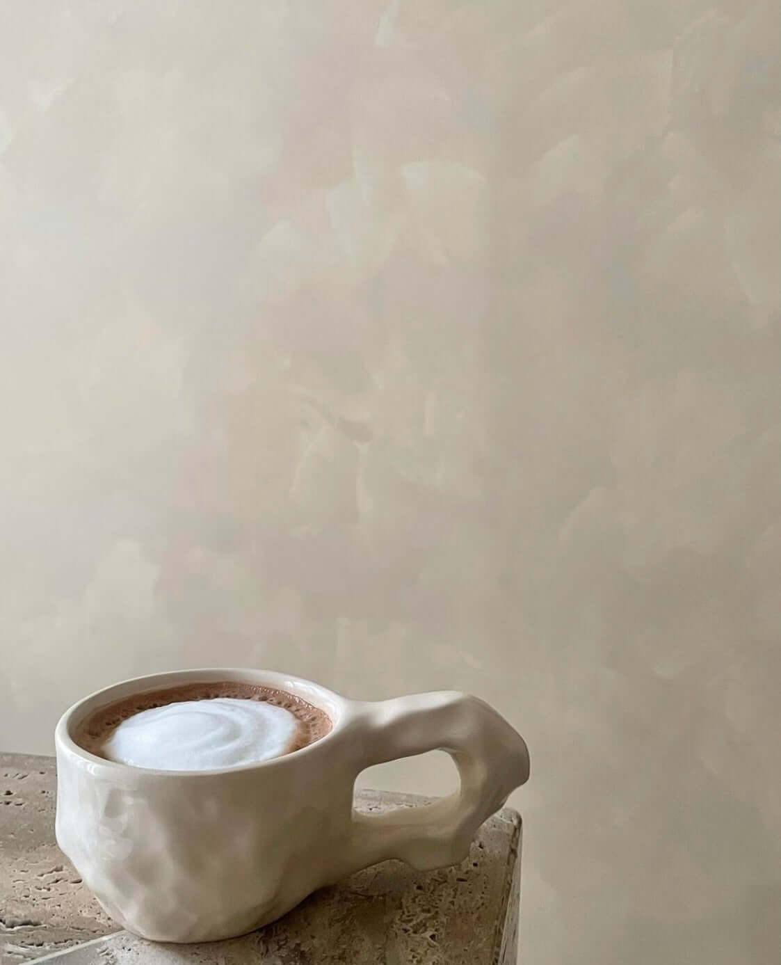 Ceramic mug with a frothy cappuccino on a marble surface against a beige background.